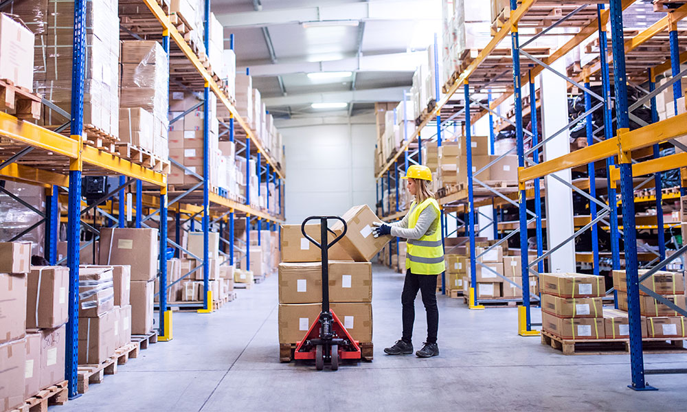 Person with a manual pallet jack in the middle of a warehouse aisle